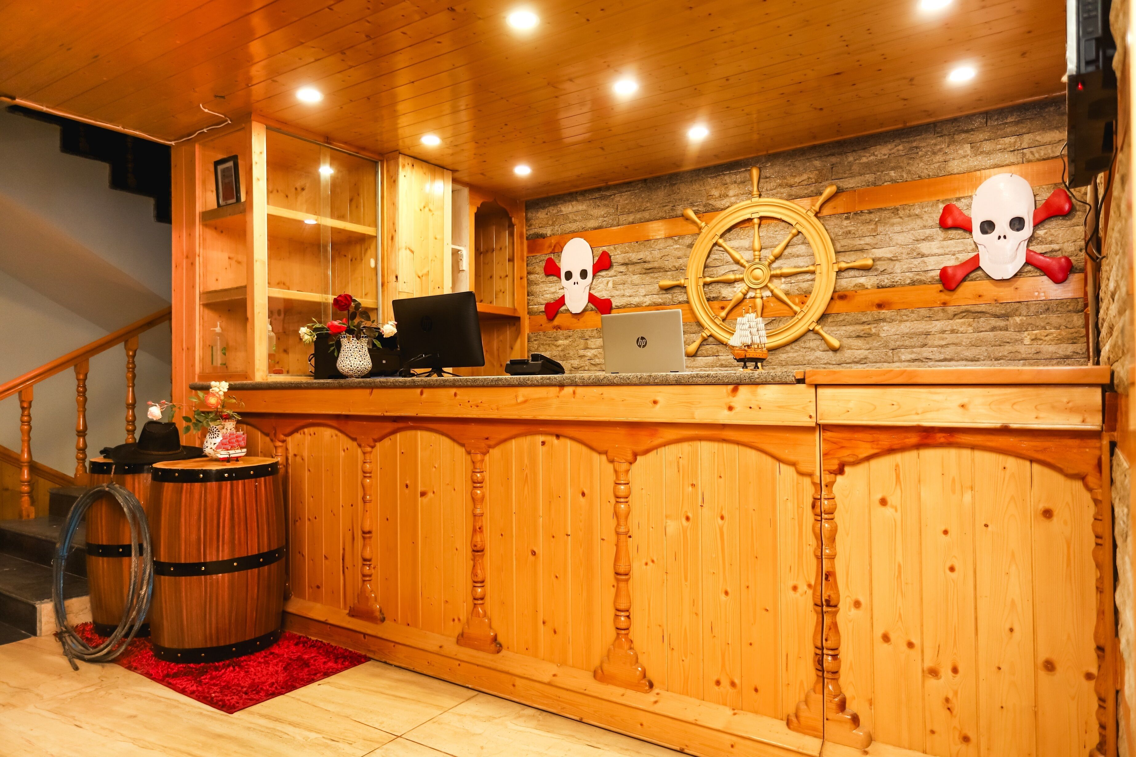 A wooden reception desk with a ship's wheel and skull decorations, a laptop, and a red rug.