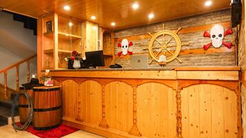 A wooden reception desk with a ship's wheel and skull decorations, a laptop, and a red rug.