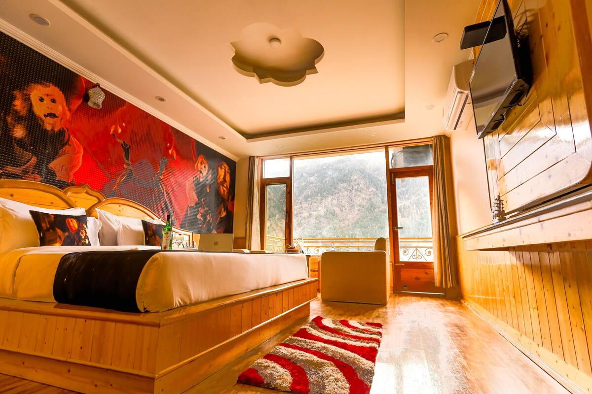 A bedroom with a large bed, a TV mounted on the wall, and a view of the outdoors through the window.