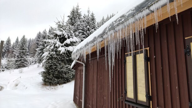 A wooden cabin with icicles hanging from the roof, surrounded by snow-covered trees. - Large vacation home on the Aschberg, great view, terrace & large garden 6+2  (Klingenthal)