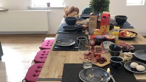 A dining table set with plates, bowls, and various food items, surrounded by cushioned seating. - Large vacation home on the Aschberg, great view, terrace & large garden 6+2  (Klingenthal)