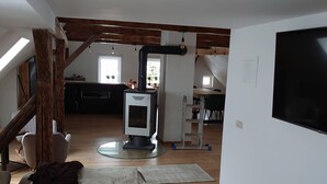 A spacious living area with a wooden table, a sofa, and a TV. There is a kitchen area in the background with a stove and a dining table. - Large vacation home on the Aschberg, great view, terrace & large garden 6+2  (Klingenthal)