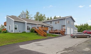 A two-story residential building with a front porch, a driveway, and a parked car. - Sleeping Lady Mountain View( The WOW Factor) Suite (Anchorage)