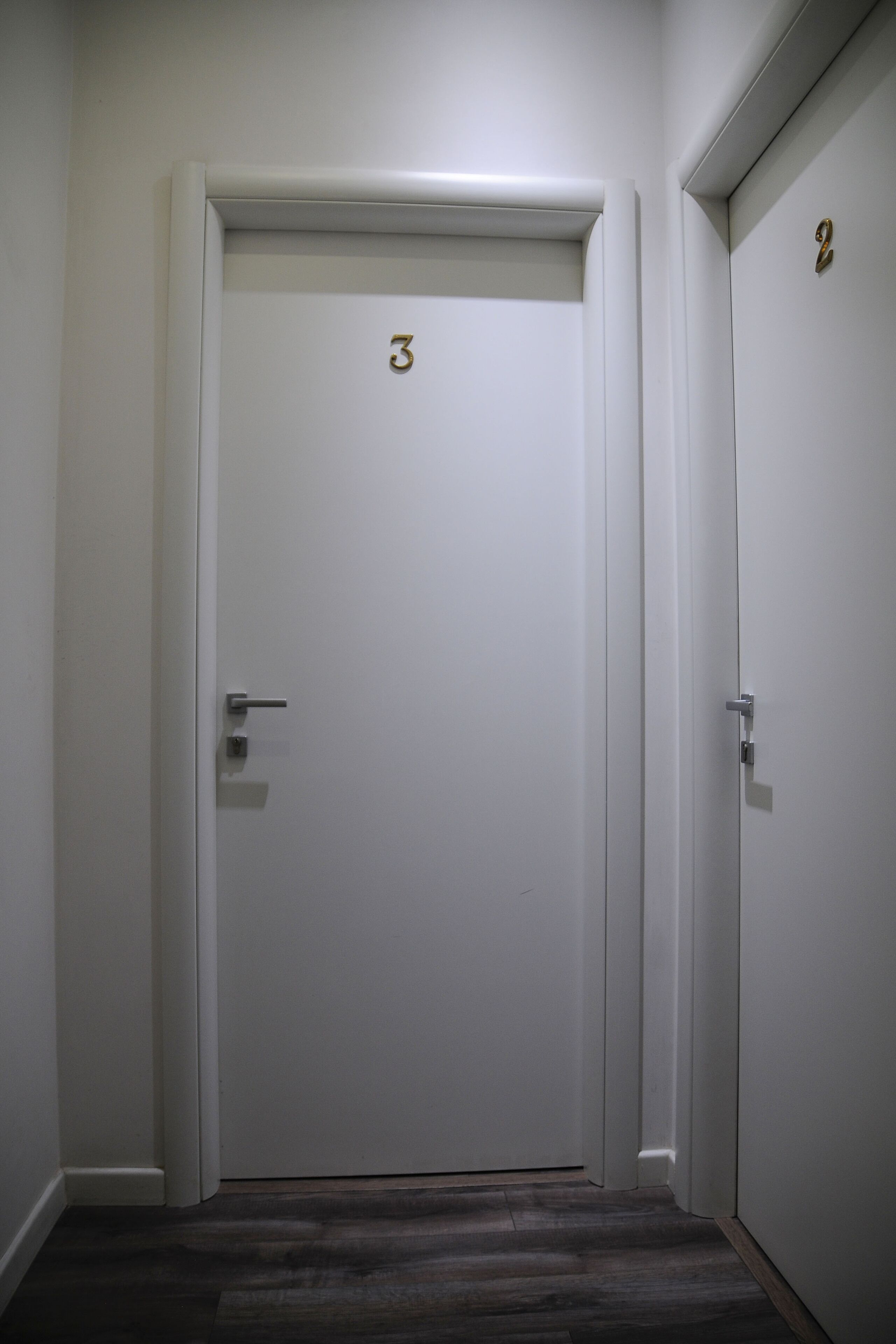 Een witte deur met het getal '3', een deurklink en een klein rechthoekig voorwerp op de deur.