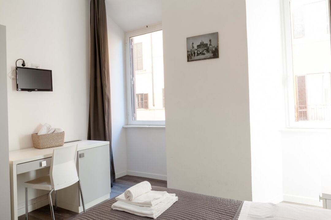 Ett hotellrum med en säng, ett skrivbord med en stol, en tv och ett fönster med gardiner.