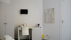 Una habitación pequeña y limpia con una cama, una mesita de noche, un espejo y un televisor montado en la pared.