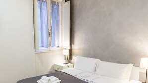 Una habitación de hotel con una cama, dos mesitas de noche, un ventanal con cortinas y una pared con textura.