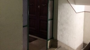 Una escalera que conduce a una puerta de madera oscura con marco verde, rodeada de paredes lisas.
