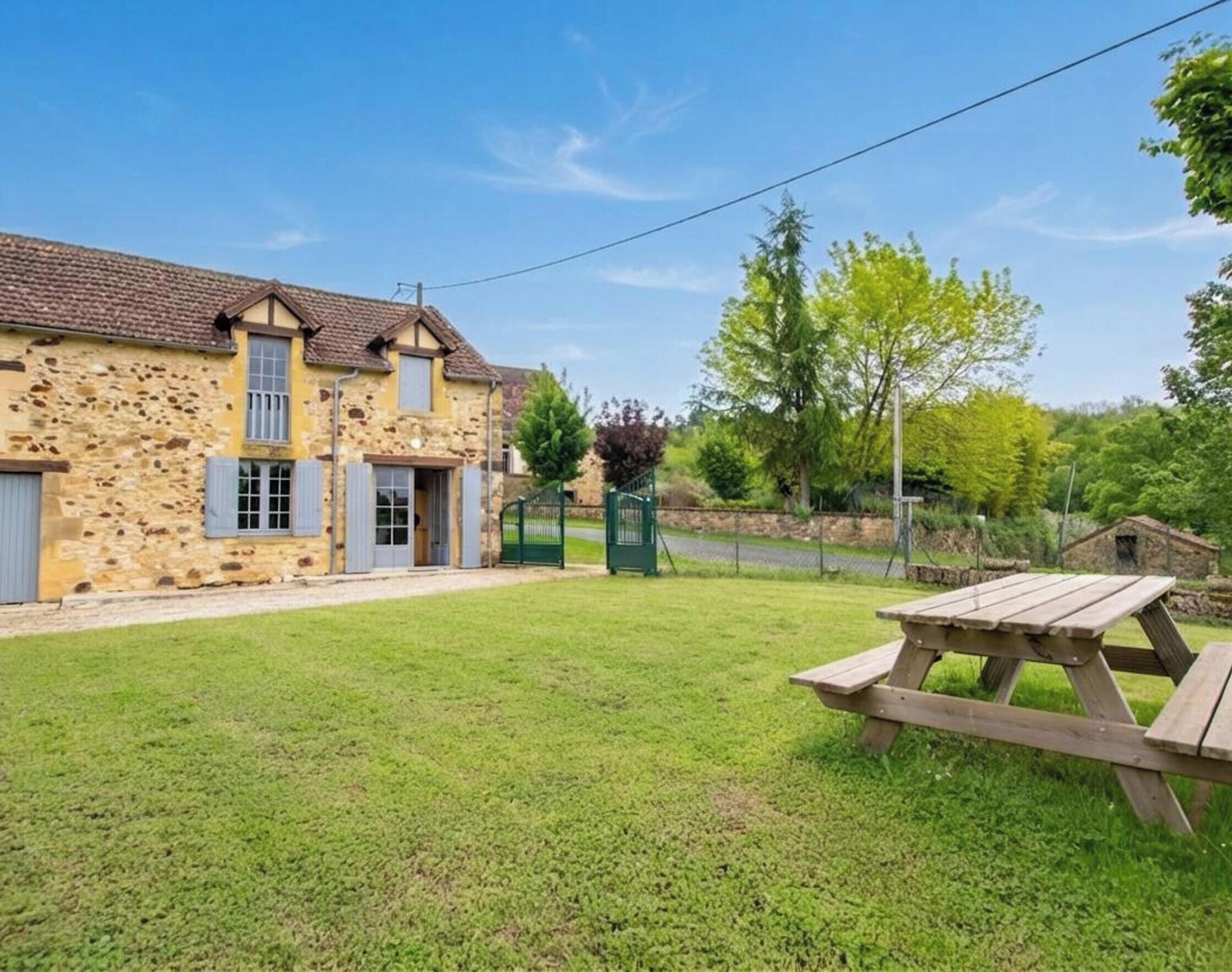 A stone building with a tiled roof, a grassy yard, and a picnic table.