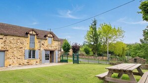A stone building with a tiled roof, a grassy yard, and a picnic table.