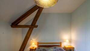 A bedroom with a sloped ceiling, a wooden bed frame, two bedside lamps, and a patterned bedspread.
