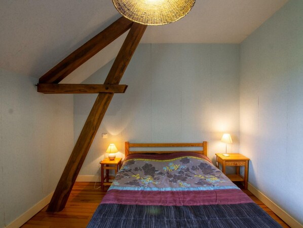 Ein Schlafzimmer mit schrägen Wänden, einem Bettgestell aus Holz, zwei Nachttischlampen und einer gemusterten Bettdecke.