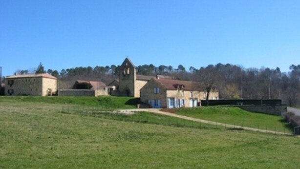 A historic building with a prominent tower, surrounded by a grassy area and a small bridge.