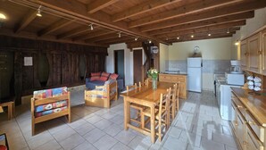 A cozy room with a wooden ceiling, a sofa, a dining table, and a kitchen area with a refrigerator and a coffee maker.