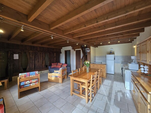 Ein gemütliches Zimmer mit Holzboden, einer Couch, einem Esstisch und einer Küchenzeile inklusive Kühlschrank und Kaffeemaschine.