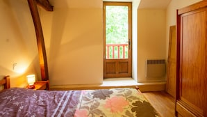 Ein Schlafzimmer mit einem Bett, einem Holzschrank, einem Fenster mit Blick ins Grüne und einer Tür mit roter Geländer.