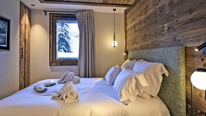 A neatly made bed with white linens and towels, a window with a view of snow-covered trees, and a wooden ceiling. - Luxury Apartment with Spa Access Near Slopes - The Allues (Méribel)