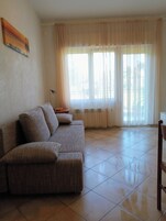 Una sala de estar con un sofá modular, una lámpara y un ventanal con cortinas traslúcidas.
