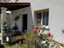 Un edificio blanco con un pilar de piedra, una pérgola de madera y una ventana con cortina.