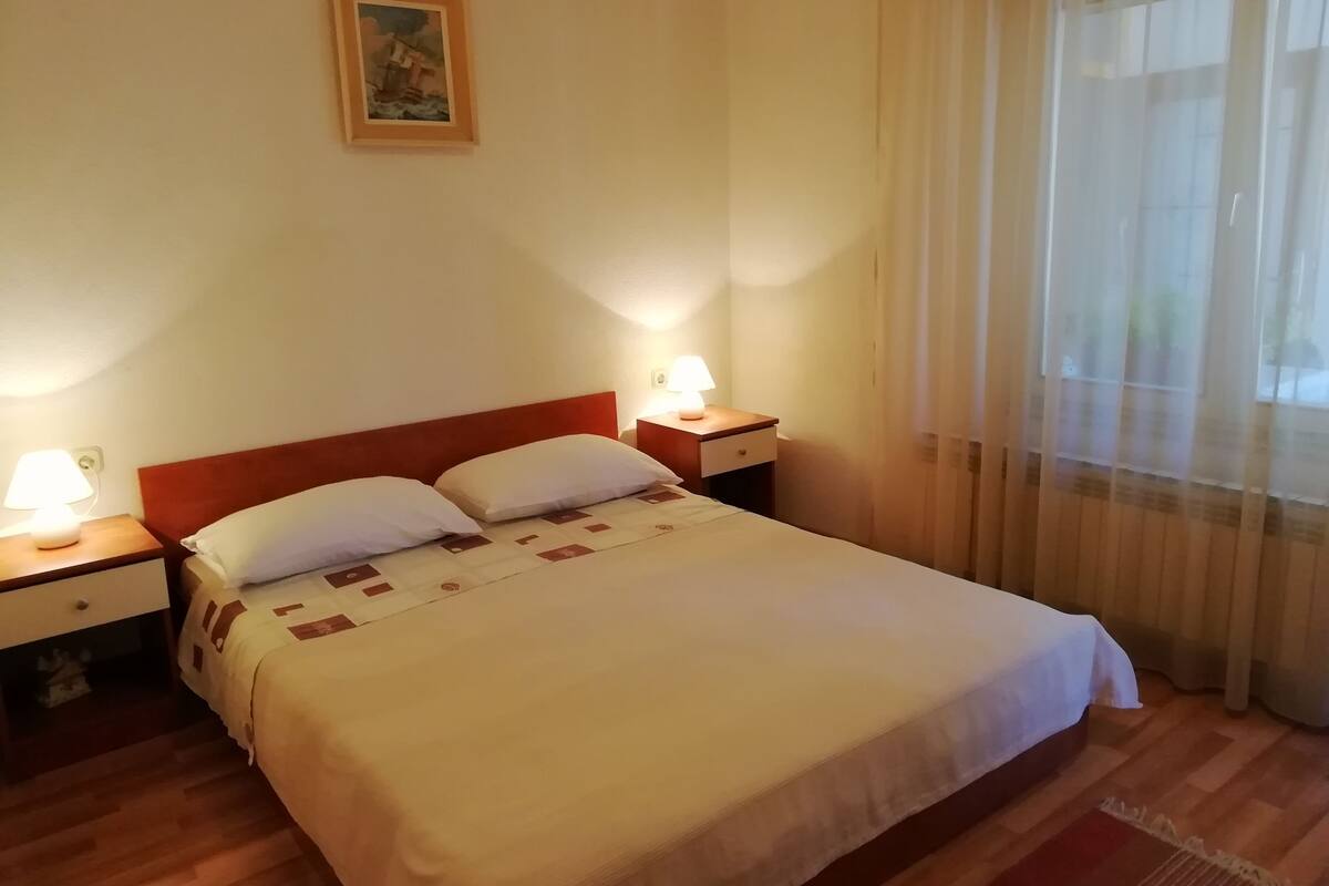 Une chambre d’hôtel avec un lit, deux tables de chevet, une lampe de chevet, un tableau au mur et une fenêtre avec des rideaux.