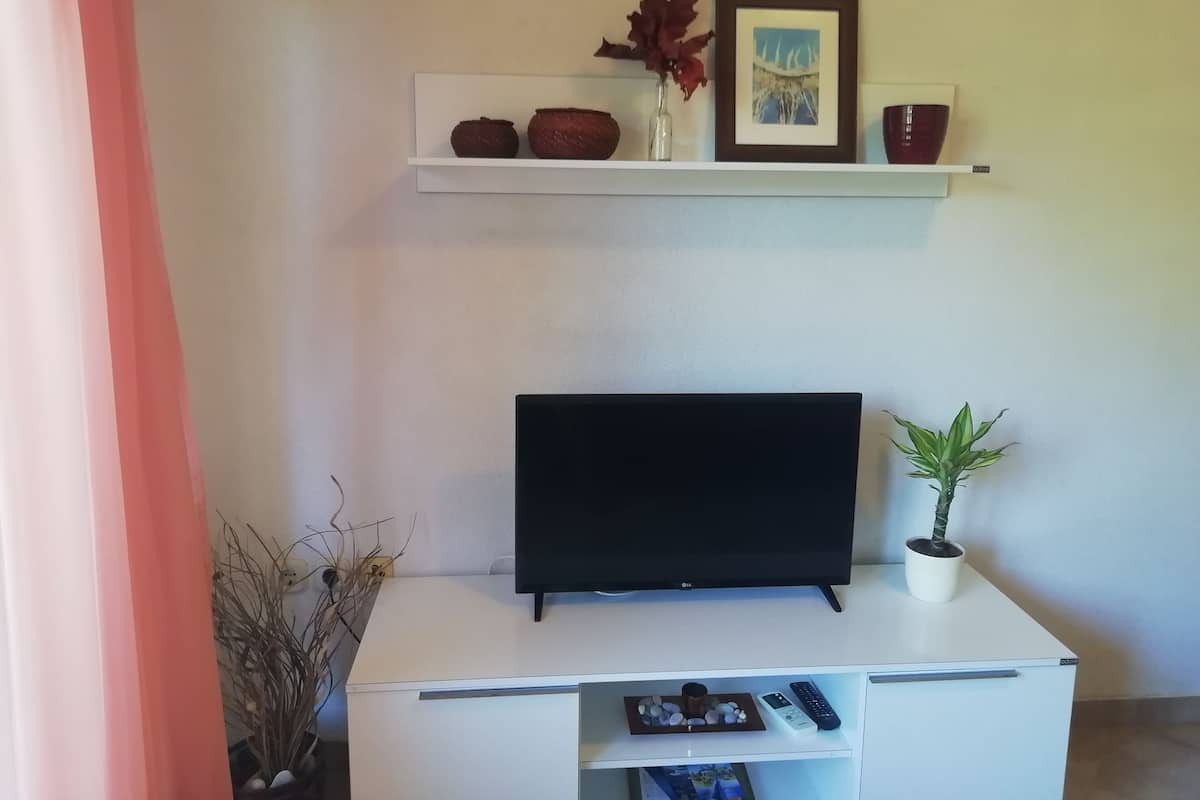 Un meuble de rangement blanc pour appareils multimédias, avec un téléviseur à écran plat, une étagère ornée d’objets décoratifs et une plante en pot.
