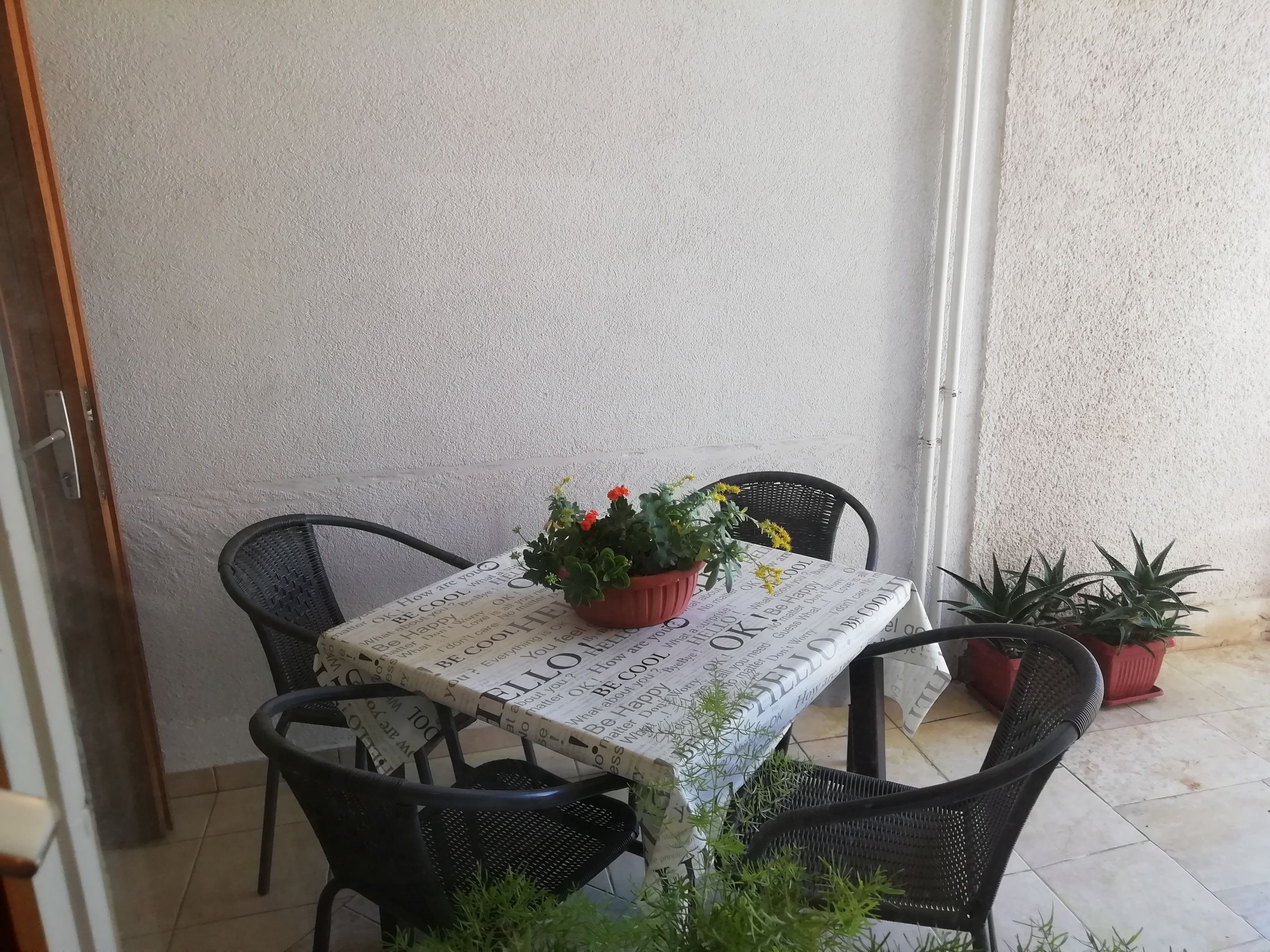 A small outdoor seating area with a table covered by a newspaper print tablecloth, surrounded by black chairs and potted plants.