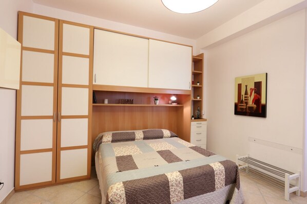 Une chambre à coucher avec un lit, une armoire, un bureau, une chaise et un tableau accroché au mur.