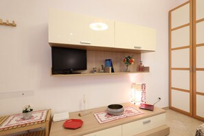 Een moderne kamer met een aan de muur bevestigde televisie, een houten tafel met een rood bord, een vaas met bloemen en een lamp.