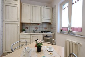 Een keuken met witte kastjes, een fornuis, een oven en een eettafel met stoelen.