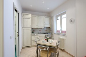 Une cuisine de taille réduite avec des meubles blancs, une cuisinière à gaz et une fenêtre avec des rideaux.