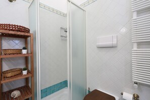 Une salle de bain équipée d’une douche, de toilettes, d’un porte-serviettes et d’une étagère avec des paniers et une plante.