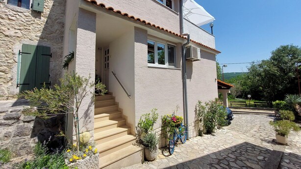Una casa de piedra con techo de tejas, una escalera que lleva a la entrada y plantas en el exterior.