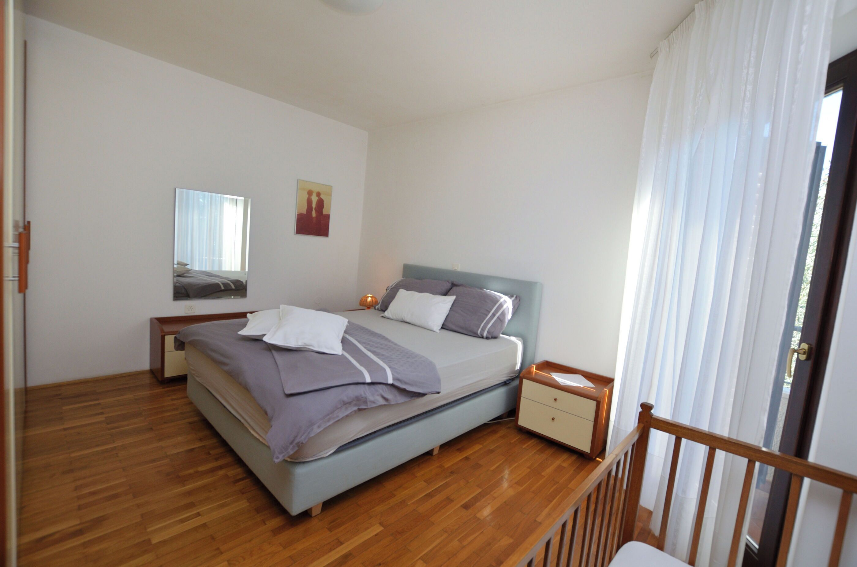 Ein Schlafzimmer mit Bett, Nachttischen, einem Spiegel und einem Fenster mit Vorhängen.