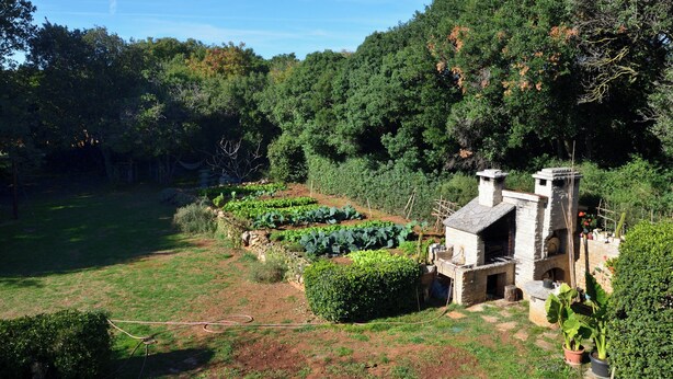 Ein rustikales Steinhaus mit Schornstein, umgeben von üppiger Vegetation und einem gepflegten Garten.