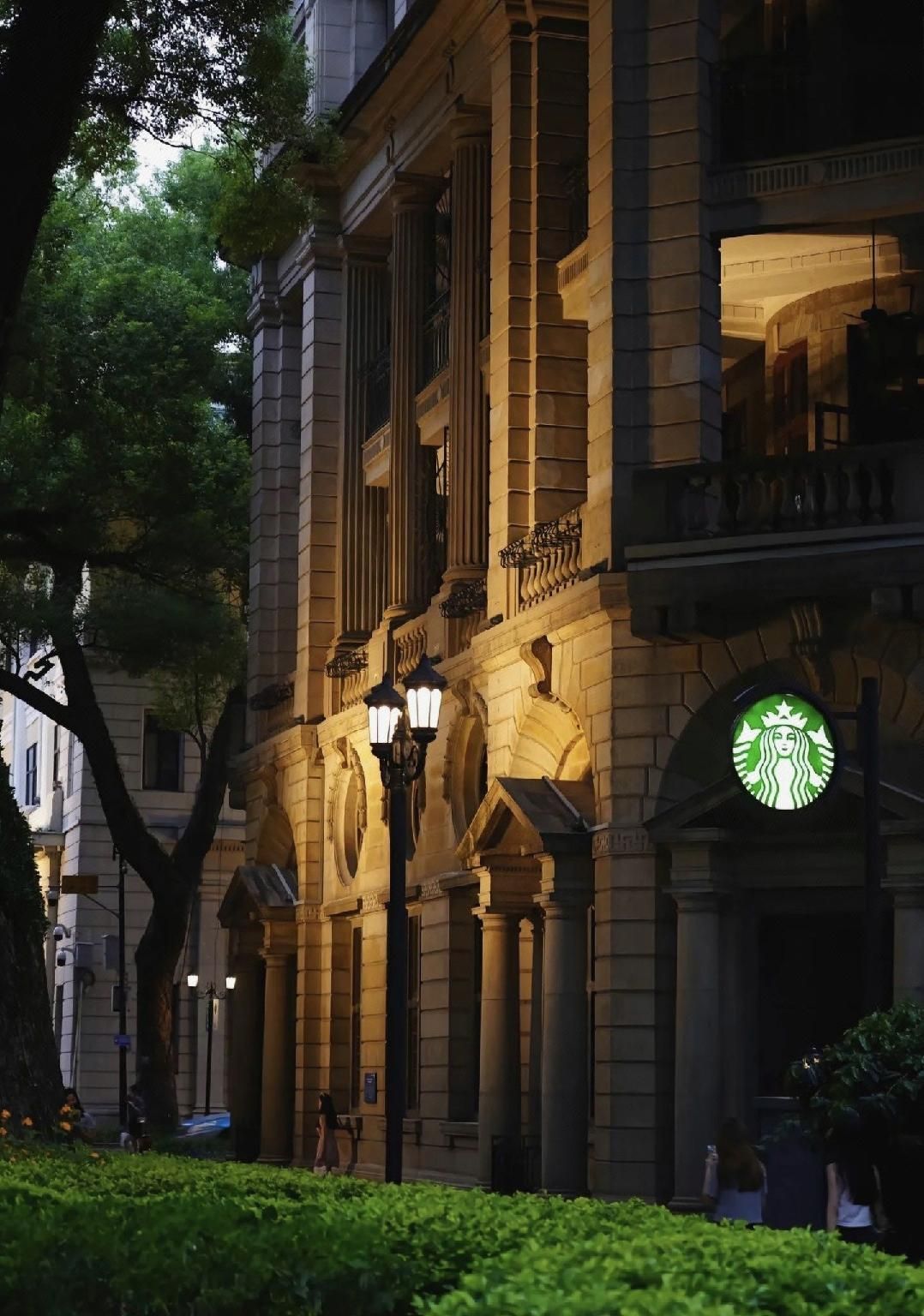 A classical building facade with columns, a Starbucks sign, and a well-maintained hedge.