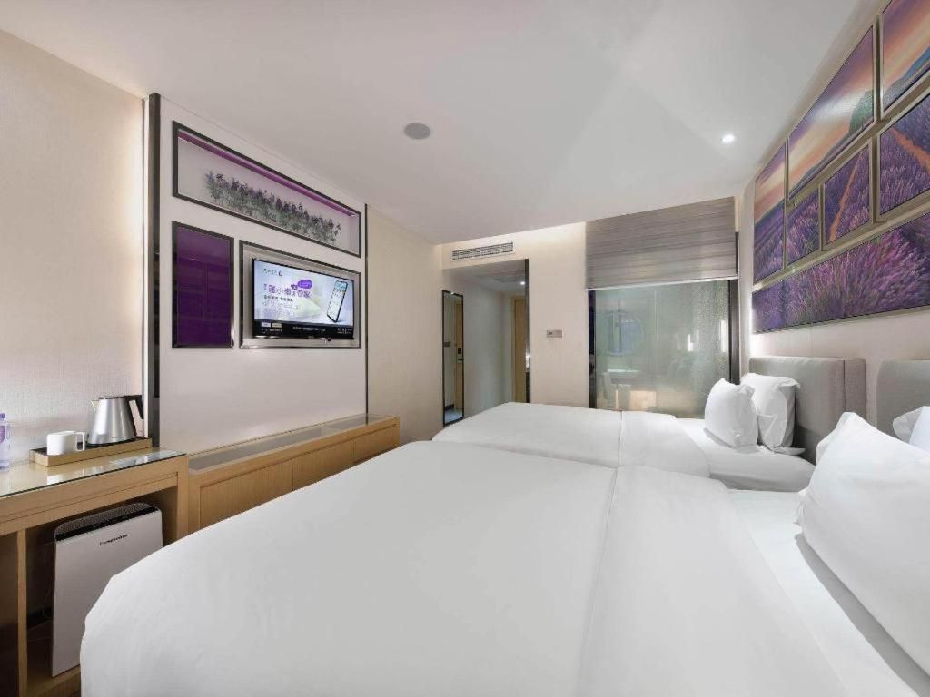 A hotel room with a large bed, a flat-screen TV, a coffee maker, and a painting on the wall.