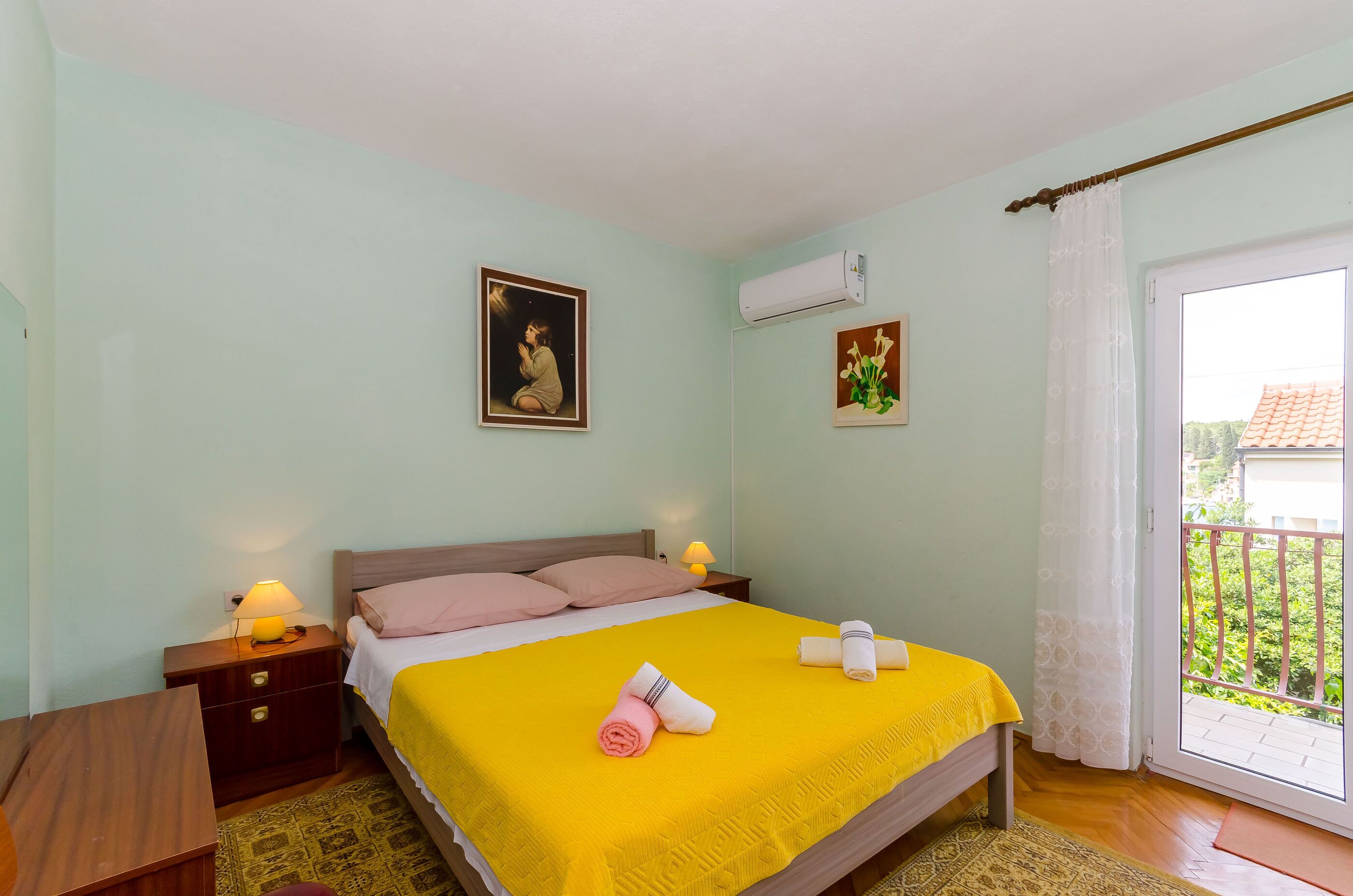 A bedroom with a bed, bedside tables, a nightstand, a window with a view, and a door.