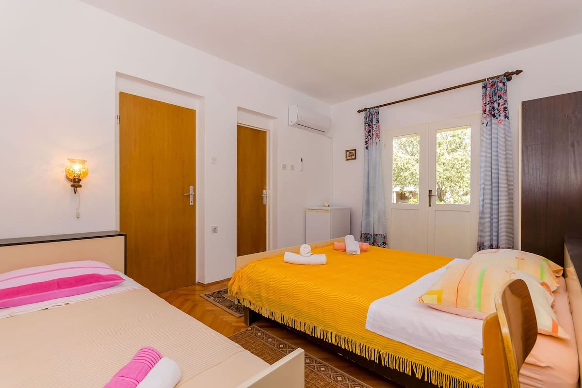 A hotel room with two beds, a wooden door, an air conditioning unit, and a window with curtains.