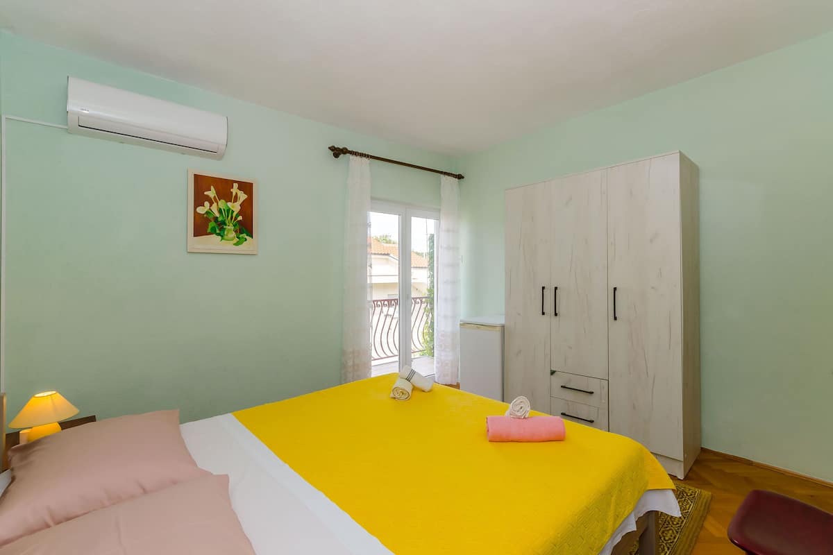 A bedroom with a bed, a wardrobe, an air conditioner, a window with curtains, and a painting on the wall.