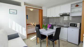 A compact kitchenette with a microwave, a sink, and a small refrigerator. There is a dining area with a table and chairs, and a bed is visible in the adjacent room.