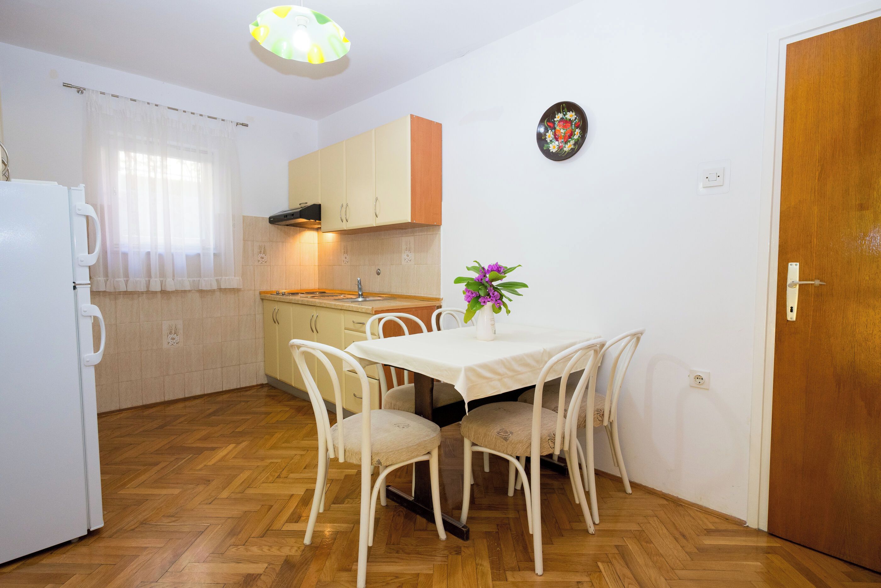 A compact kitchen with a dining table, chairs, a refrigerator, and a wooden floor.
