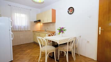 A compact kitchen with a dining table, chairs, a refrigerator, and a wooden floor.
