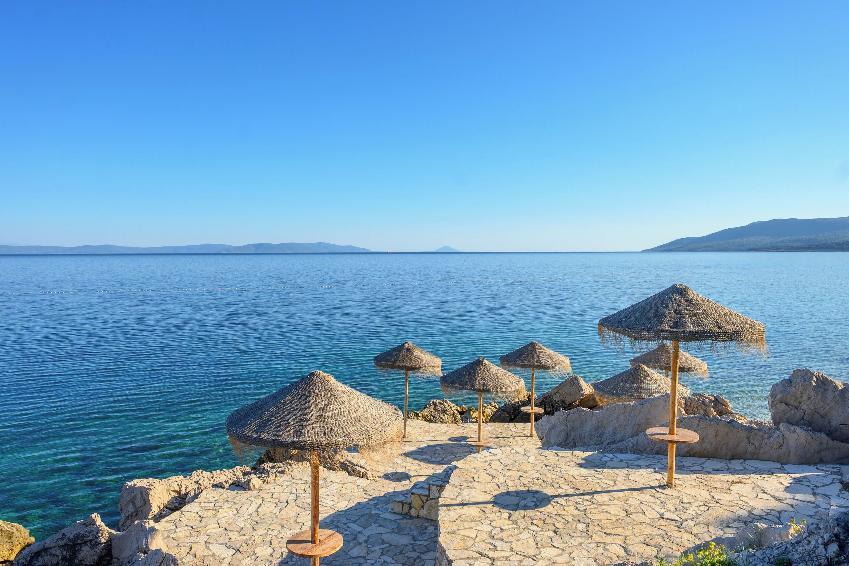 Un paysage côtier avec une zone pavée de pierres et des parasols en chaume.