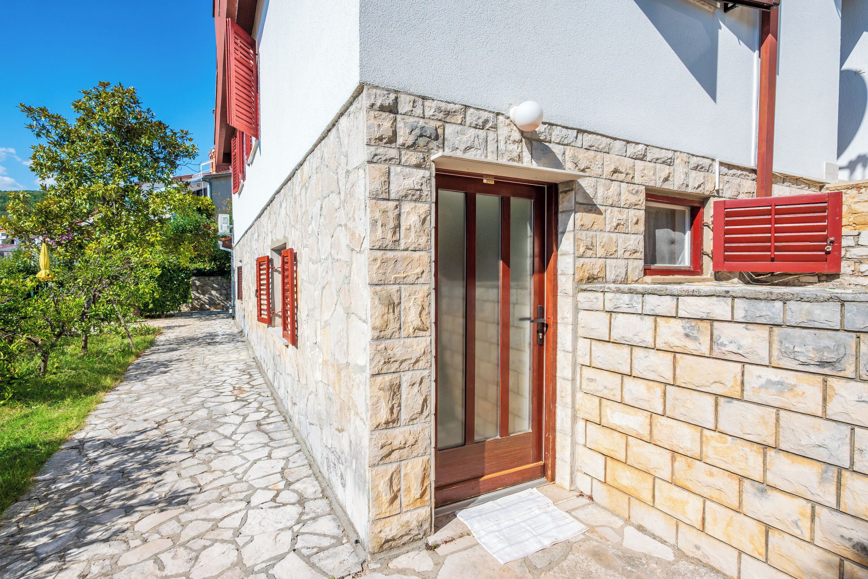 A stone building with a wooden door and shutters, a stone pathway, and a small window.