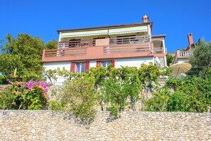 Un bâtiment à deux étages, avec un mur de pierre à l’avant, un balcon à l’étage supérieur et un ciel d’un bleu limpide.