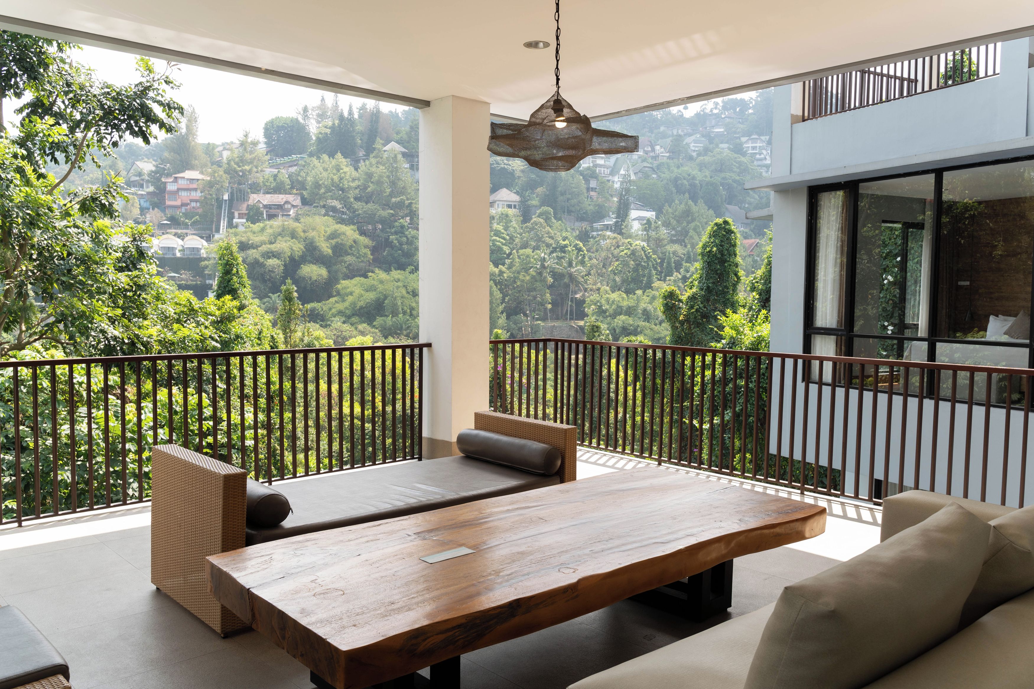 A modern balcony with a wooden table and seating, overlooking a lush green landscape.