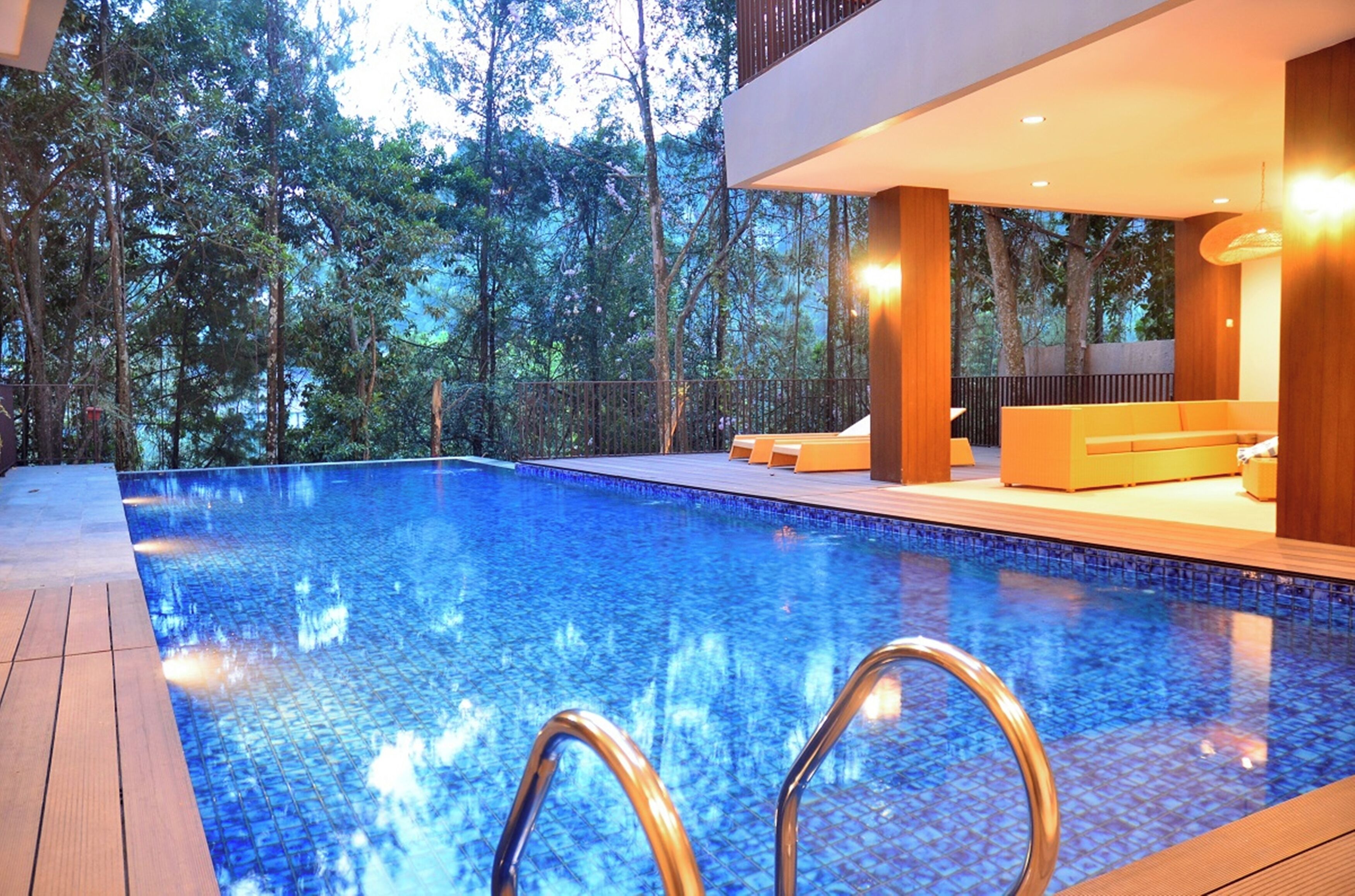 Una piscina con cubierta de madera y sillones de descanso, rodeada de árboles.