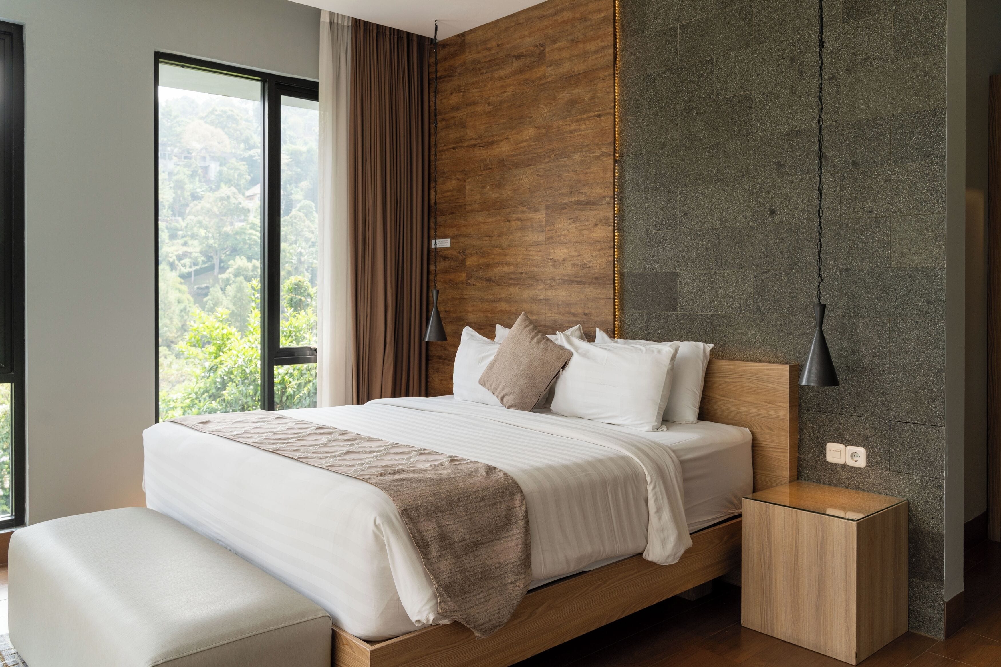 Un dormitorio moderno con una cama grande, cabecera de madera, una mesita de noche y vistas al exterior.