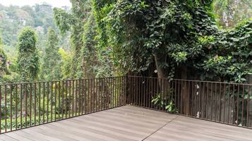 Eine Holzterrasse mit Metallgeländer, umgeben von dichtem Grün und Bäumen.