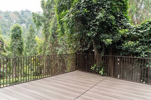 Une terrasse en bois avec une rambarde en métal, entourée d’une végétation luxuriante et d’arbres.
